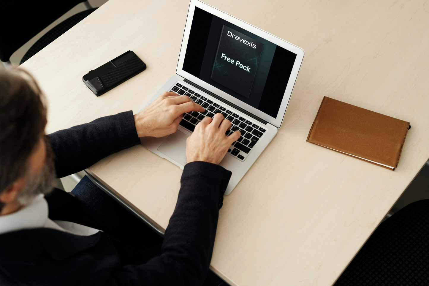 Person using a laptop on a desk with a phone and notebook nearby